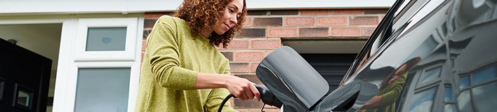 Woman charging electric vehicle at a charging station.