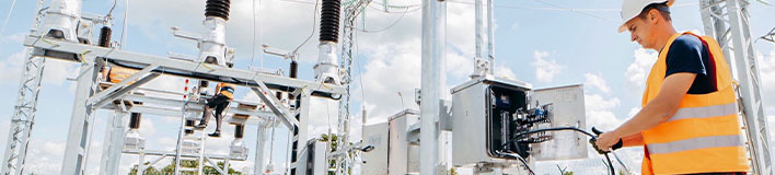 Worker operates equipment at power station, another works on overhead lines.