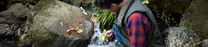 Man collects water sample with handheld instrumentation device.