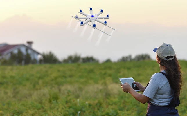 Farmer operating a tablet controller, monitoring a large multi-rotor drone watering a grassy field.